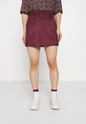 Bordeauxfarvet ruskind mini nederdel med en glat tekstur, der har taljeret pasform og diskrete syningsdetaljer, kombineret med hvide ankelstøvler.