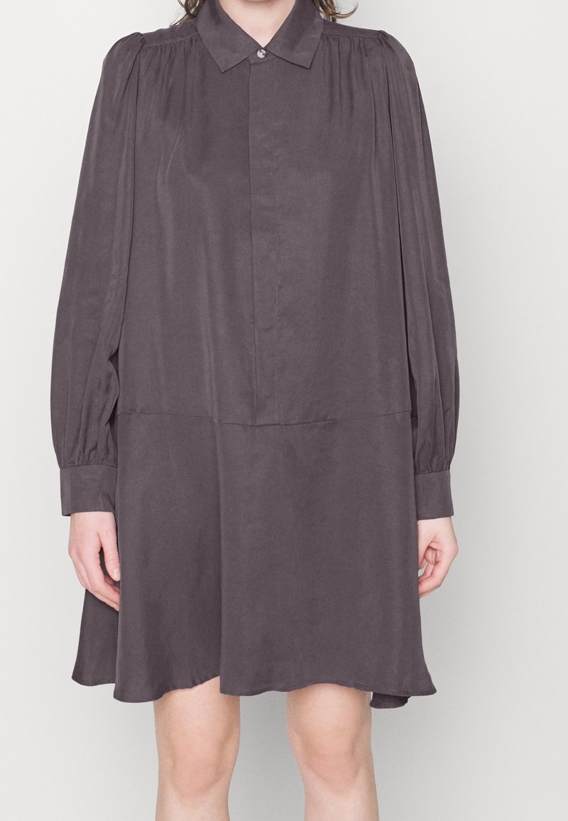 Abito camicia grigio scuro con colletto, maniche lunghe e vestibilità comoda. Realizzato in tessuto liscio con una leggera finitura lucida. Chiusura con bottoni.