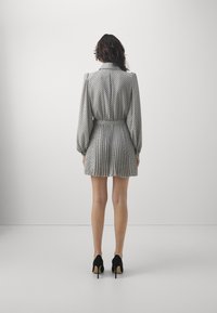 Vestito a maniche lunghe in grigio chiaro con pois neri, vita aderente, gonna plissettata e colletto alto. Lunghezza della gonna sopra la metà della coscia. Scarpe con tacchi neri.