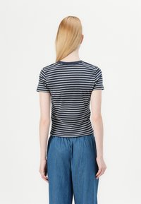 Navy and cream striped short-sleeve t-shirt with a round neckline, paired with loose-fitting blue denim pants. Smooth cotton texture.