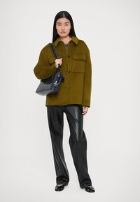 Olive green oversized wool-blend jacket with two chest pockets, paired with black faux leather trousers and a black handbag. Striped top visible.