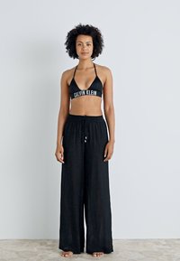 Crni trokutasti bikini gornji dio s logom "Calvin Klein", uparen s širokim crnim hlačama na vezanje. Glatka tekstura, ležeran dizajn.