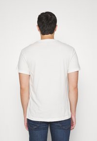 Weiße Baumwoll-T-Shirt mit kurzen Ärmeln, Rundhalsausschnitt und einem schlichten Rücken. Kombiniert mit blauen Denim-Jeans, die eine lässige Passform zeigen.