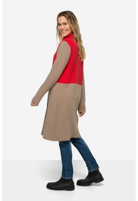 Cardigan fino a ginocchio con la parte superiore rossa e la parte inferiore beige. Maniche lunghe, texture a coste, abbinato a jeans blu e stivali neri alla caviglia.