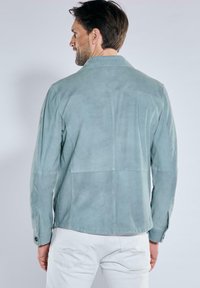 Wildlederjacke in hellblau-grün, strukturiertes Design mit spitzem Kragen und geknöpften Manschetten, mit glatter Textur und gesteppten Details.