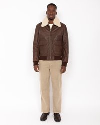 Chaqueta de cuero marrón con cuello de borreguito sintético crema, bolsillos frontales y puños acanalados, combinada con pantalones de pana beige y zapatos marrones.