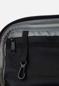 Svart tygficka med dragkedja som har en grå inredning, YKK-dragkedja och en fäst svart elastisk rem med en krok för att säkra föremål.