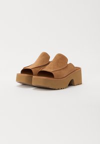 Bruine suede open teen mules met een brede bovenkant en een chunky plateauzool. Geprofileerde buitenzool biedt grip. Eenvoudig ontwerp, geen zichtbare hardware.