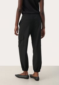 Zwarte cargo broek met elastische tailleband en boorden, met zijzakken en een knoopcargo zak op het linkerpijp. Glad stoftextuur.
