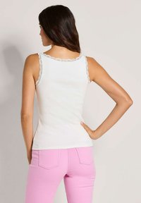 Weißes, geripptes Tanktop mit Spitzenbesatz entlang des Halsausschnitts und der Träger, getragen mit rosa, enganliegenden Jeans, die eine schlanke Silhouette bieten.