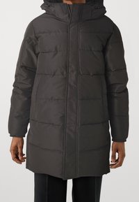 Cappotto lungo nero imbottito con cappuccio, caratterizzato da una texture trapuntata, zip frontale e tasche laterali. Materiale robusto con un design elegante.