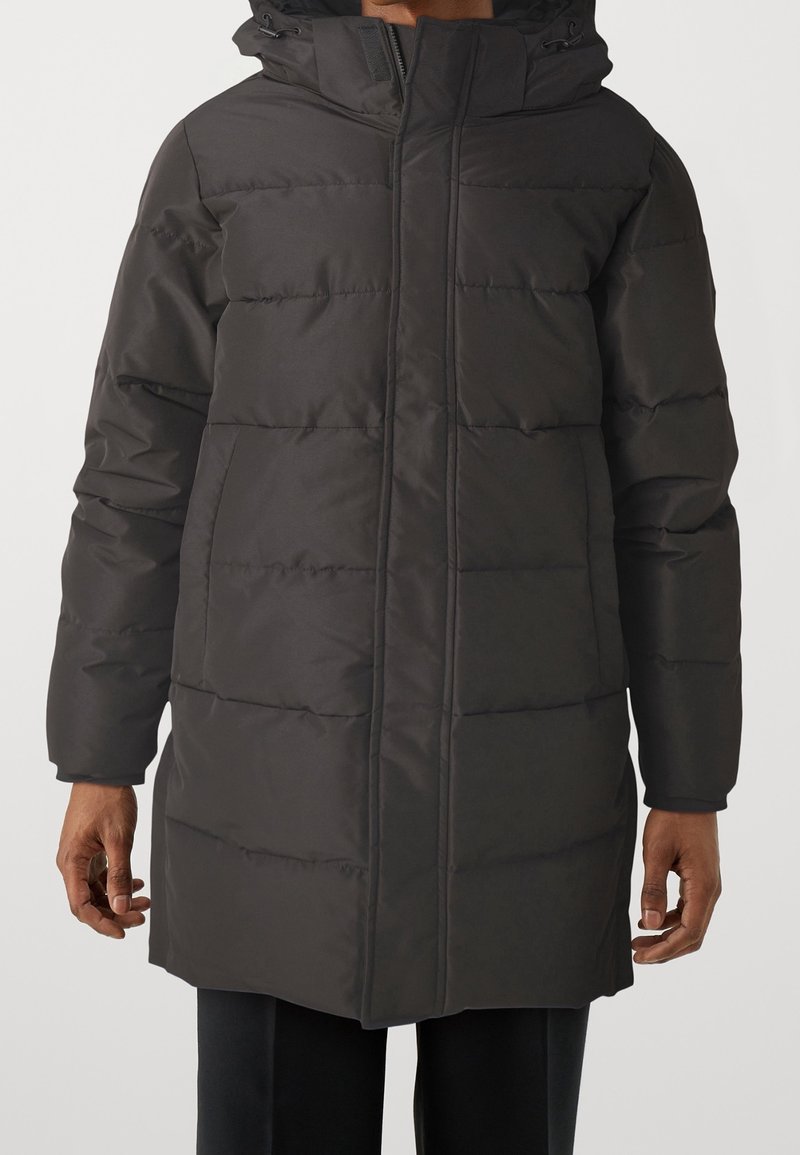 Cappotto lungo nero imbottito con cappuccio, caratterizzato da una texture trapuntata, zip frontale e tasche laterali. Materiale robusto con un design elegante.