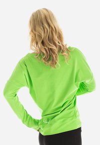 Top vert à manches longues avec une coupe ample, fabriqué dans un tissu léger. Présente un ourlet incurvé et un détail de logo dans le bas du dos.