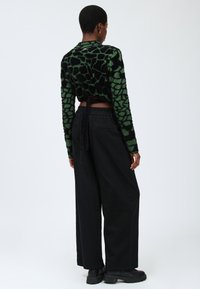 Grüner und schwarzer flauschiger, cropped Pullover mit einem strukturierten, geometrischen Muster. Kombiniert mit lockeren schwarzen Hosen und klobigen schwarzen Stiefeln.