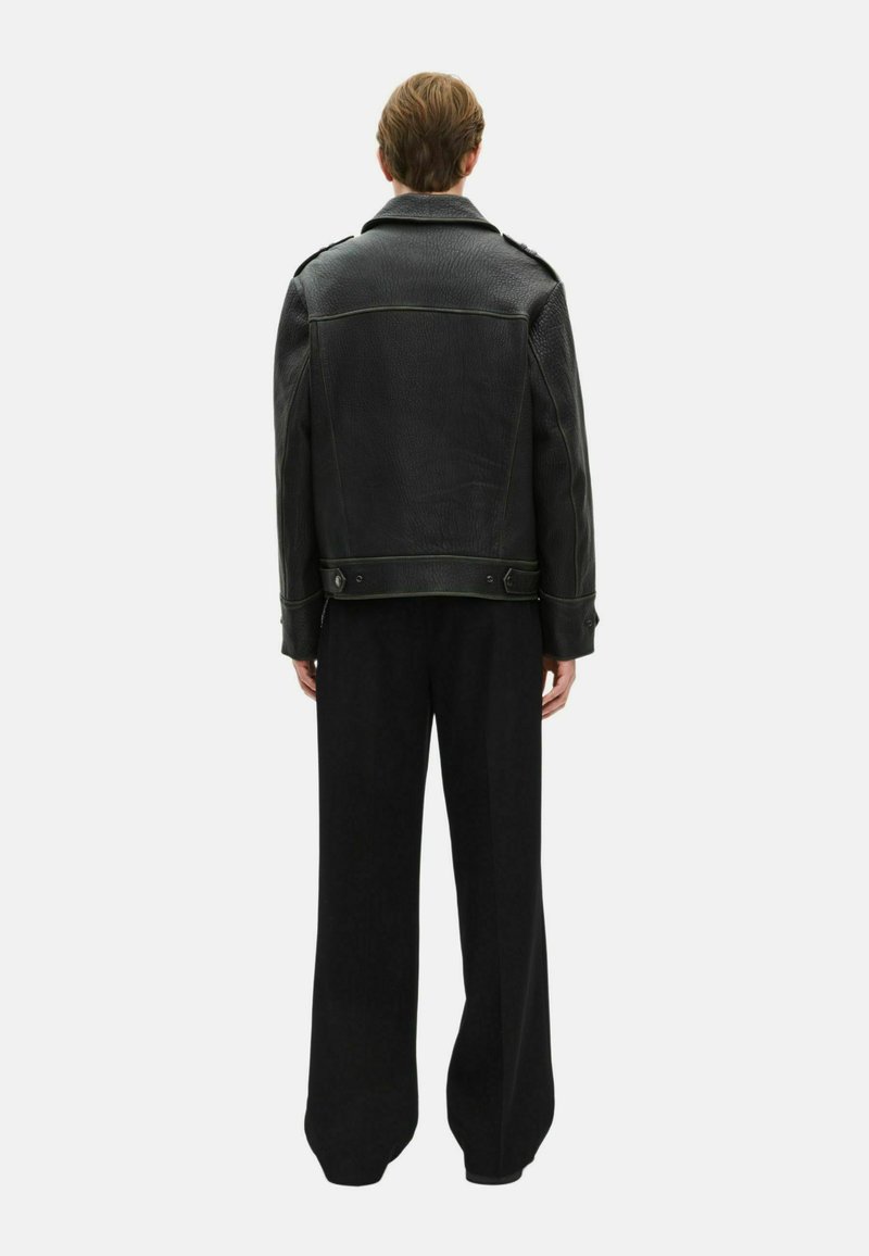 Veste en cuir noir avec une finition texturée, dotée d'un large col, de coutures contrastantes et de détails à boutons-pression. Associée à un large pantalon noir.
