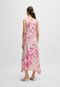 Ärmelloses Kleid aus leichtem Stoff mit einem rosa Blumenmuster. Asymmetrischer Saum, fällt unter das Knie und wird mit beigefarbenen, geschnürten Sandalen kombiniert.