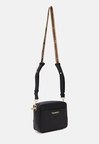 Czarna torba na ramię wykonana z gładkiego materiału syntetycznego, o prostokątnym kształcie, z zamkiem błyskawicznym i markowym paskiem z złotymi akcentami.