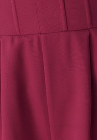 Tela color granate con pliegues y textura suave. El diseño es sencillo, con una silueta ligeramente fluida, adecuada para diversas ocasiones.