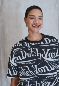 Black t-shirt with large white "Von Dutch" logo print, short sleeves, crew neck, relaxed fit, soft fabric. Gold heart-shaped earrings.