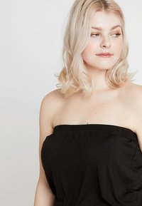 Svart axelbandslös topp i mjukt tyg med en samlad elastisk band. Slät textur, skräddarsydd design och en enkel, minimalistisk stil.