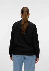 Czarny sweatshirt z okrągłym dekoltem, ściągaczami przy rękawach i hemie. Noszony z jasnoniebieskimi dżinsami, widok od tyłu. Gładka tekstura.