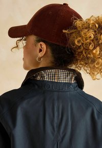 Jachetă de marină cu guler din catifea, având un model în carouri maro și bej. Cappă din catifea maro și cercuri de ureche vizibile.