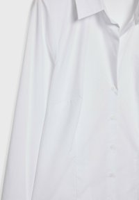 Chemise blanche à boutons avec col. Manches longues, texture lisse, dotée de poches latérales cachées et d'une coupe classique.