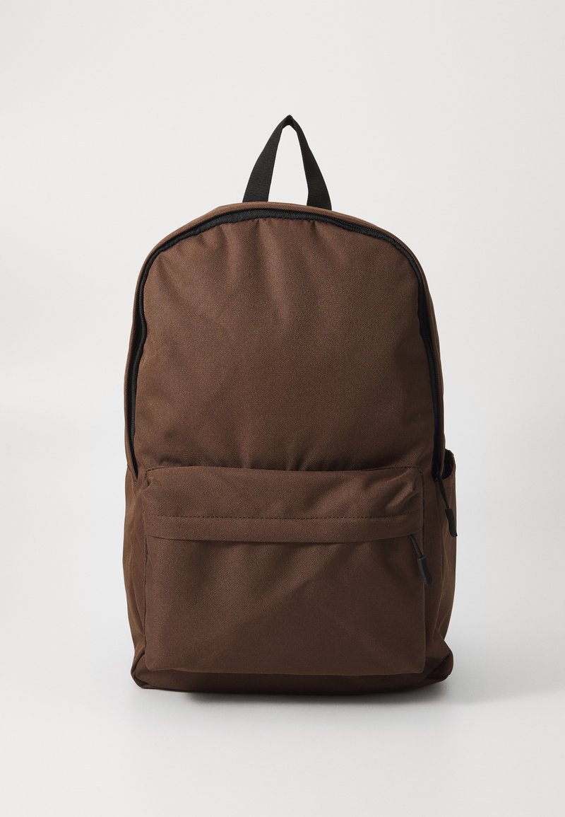 Mochila de tecido castanho com fecho de correr, um bolso frontal e uma pega em cima. Apresenta uma forma estruturada e uma textura subtil.