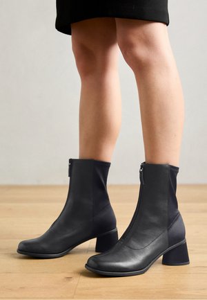 Zwarte enkellaarsjes met een gemengd materiaald ontwerp, featuring glad leer en rekbare stof, een vierkante neus en een blokhak van gemiddelde hoogte.