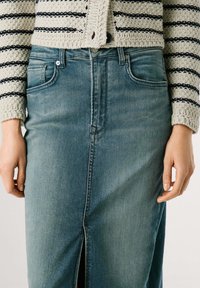 Lichtblauwe spijkerrok met een rechte snit, met een split aan de voorkant. Gekocht met een textuur, cremekleurige en marineblauwe gestreepte gebreide cardigan.