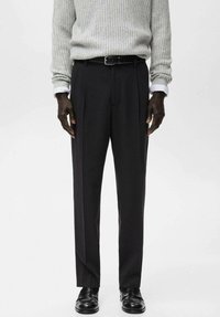 Pantaloni neri su misura con gamba dritta e pieghe frontali, abbinati a un maglione grigio chiaro a coste e scarpe di pelle nere.