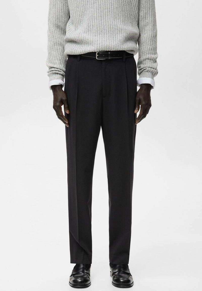 Pantaloni neri su misura con gamba dritta e pieghe frontali, abbinati a un maglione grigio chiaro a coste e scarpe di pelle nere.