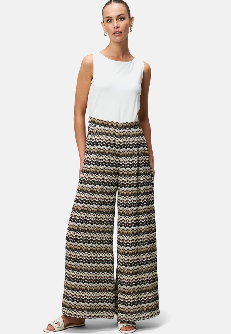 Un pantalon large à motifs dans un design ondulé marron, noir et blanc, associé à un haut sans manches ajusté blanc et des sandales légères.
