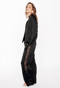 Ensemble de pyjama en satin noir avec des accents en dentelle sur les côtés du pantalon, comprenant une chemise à manches longues avec boutons et un pantalon à coupe décontractée.