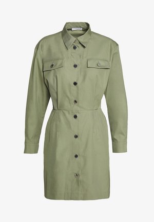 Jasnozielona sukienka koszulowa na guziki z długimi rękawami, dwoma kieszeniami na piersi z klapkami i guzikami oraz szpiczastym kołnierzem.
