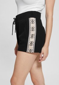 Pantaloni neri con vita alta, caratterizzati da una striscia laterale beige con un motivo intricati e dettagli con cordino regolabile.