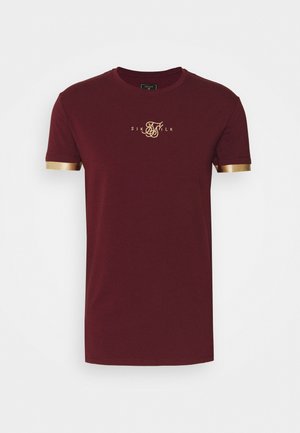 Bordowa koszulka z krótkim rękawem, ze złotym wykończeniem na rękawach i złotym logo "Sik Silk" na środku klatki piersiowej.