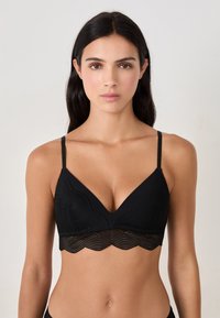Reggiseno nero con orlo in pizzo a scallop, caratterizzato da un design a V e spalline sottili e regolabili. Tessuto strutturato con motivi a onda.