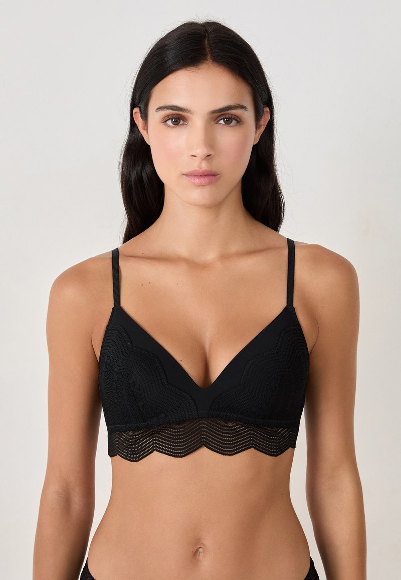 Reggiseno nero con orlo in pizzo a scallop, caratterizzato da un design a V e spalline sottili e regolabili. Tessuto strutturato con motivi a onda.