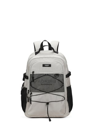 Zaino grigio chiaro con molteplici scomparti con cerniera, tasca frontale in rete nera, spallacci regolabili e dettaglio con cordoncino elastico sul davanti.