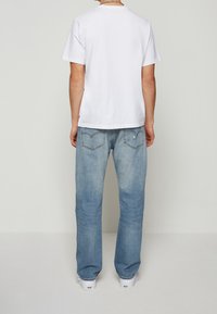 Bílá bavlněná tričko s kulatým výstřihem, v kombinaci se světle modrými džíny s volným střihem a mírným opotřebením.