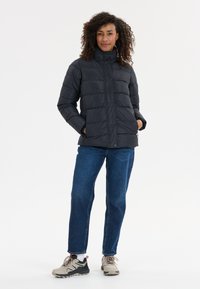 Dunjacka i mörkgrått med hög krage, knäppning och quiltat mönster. Kombinerad med blå denimjeans och neutrala träningsskor.