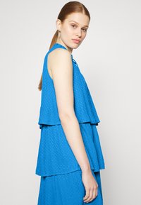 Top azul sem mangas com design em camadas, tecido texturizado e decote com franzido. O top apresenta um corte solto e um padrão subtil.