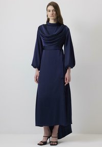 Rochie lungă de culoare albastru închis, cu un front drapat și mâneci tip clopot; are o talie ajustată și o fustă cu margine asimetrică; țesătură fină și ușoară.
