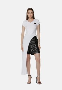 Biały T-shirt z dekoltem w serek i długim bocznym panelem; połączony z czarnymi, błyszczącymi, plisowanymi szortami. W zestawieniu ze strapowanymi czarnymi szpilkami, minimalne czarne akcenty.