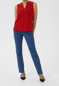 Top rosso senza maniche con scollatura a V, design testurizzato, abbinato a jeans slim-fit blu e scarpe col tacco a punta nere. Look semplice e sartoriale.