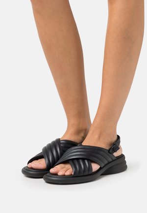 Black leather sandals with crisscross straps and ribbed texture, featuring an adjustable strap and a cushioned sole for comfort.