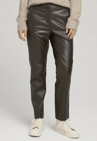 Bruna läderbyxor med en slät yta, med en skräddarsydd passform, vertikala sömdetaljer, och parades med vita sneakers.