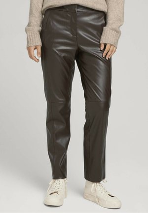 Pantalons en cuir brun avec une texture lisse, présentant une coupe ajustée, des détails de couture verticaux, et associés à des baskets blanches.