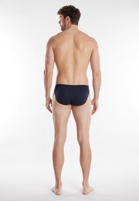 Slips de bain navy fabriqués �à partir d'un matériau léger, présentant un design simple avec une taille basse et une texture lisse, vus de l'arrière.